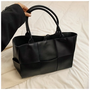 Detailed top view of black woven leather tote bag featuring wide strap interlacing technique