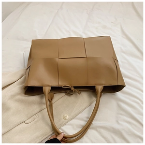 Detailed top view of large camel woven leather tote bag on textured background