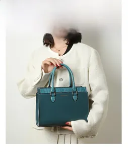Front view of model carrying a dark teal tote bag with crocodile texture details
