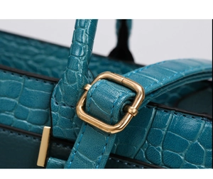 Detailed macro view of dark teal crocodile embossed leather with a gold metal buckle