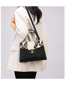 Fashionable black faux leather handbag with snake print flap and gold clasp on a model