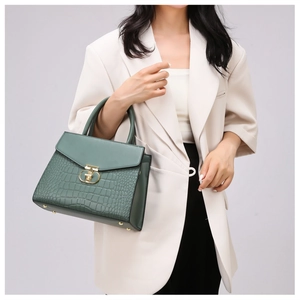 Detail of dark green crocodile pattern handbag with gold clasp on beige suit model