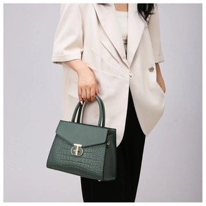 Detail of dark green handbag with faux crocodile texture and gold clasp held by model