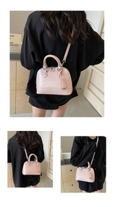 Detail showing the pink crocodile pattern texture and metal zipper on the shell handbag