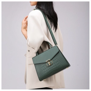 Detail of dark green crocodile texture handbag worn by a model in a beige suit