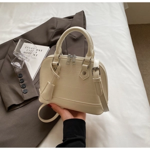 Detailed view of cream crocodile embossed texture on a shell-shaped crossbody bag
