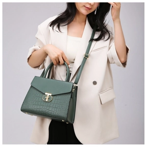 Detail of dark green shoulder bag with crocodile texture and gold T-lock shown on a model