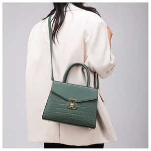 Detail of dark green crocodile texture handbag with gold T-shaped lock on beige blazer
