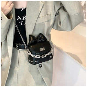 Black mini box bag with 3D bow and silver chain strap shown on a gray blazer suit