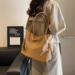 Detail of a khaki nylon tote bag with brown leather handles and a long front zipper pocket