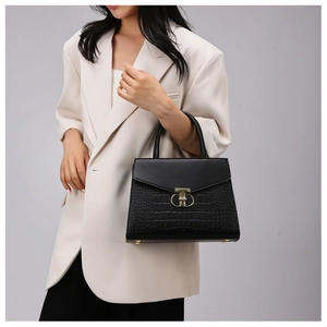Detail of black faux crocodile texture handbag with gold circular metal buckle on model