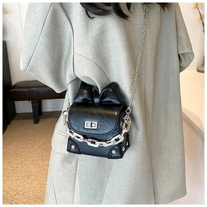 Detail of black bow square bag featuring silver chain and textured leather on grey blazer