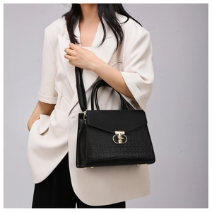 Detail of black crocodile pattern textured handbag featuring a gold T-bar metal clasp