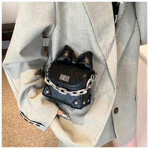 Detail of black glossy crossbody bag with large bow, silver chain and metal lock