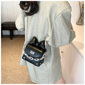 Detail view of mini black crossbody bag with large bow and silver chain on model