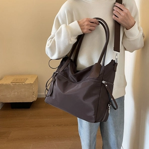 Close-up of large dark brown tote bag with leather trim and wide fabric shoulder strap