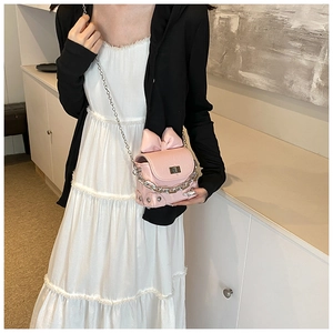 Detailed view of pink bow box bag with silver metal lock and chain strap on a white dress