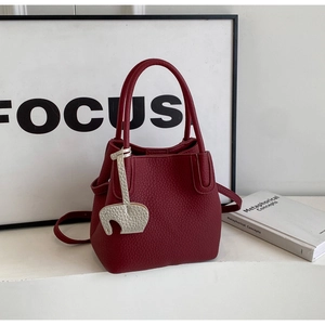 Detail of burgundy bucket bag featuring lychee texture and white horse charm accessory