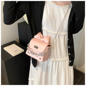 Pink mini crossbody bag with bow detail and chain strap worn by a model in a dress