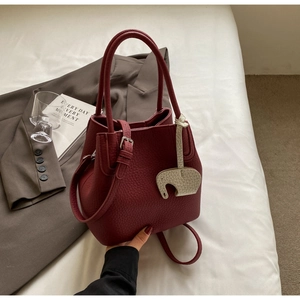 Detail of burgundy bucket bag with litchi texture and cute ivory elephant charm