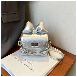 Detailed close-up of silver mini bow box bag with metallic texture on white book