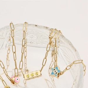 Détail de colliers à maillons dorés avec pendentifs étoile et œil maléfique rose et bleu