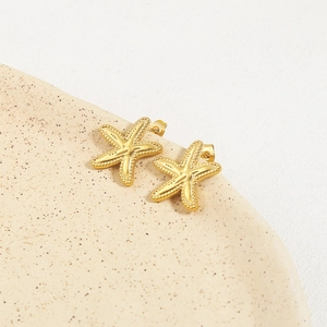 Golden starfish stud earrings with beaded texture on a ceramic tray, ocean theme jewelry