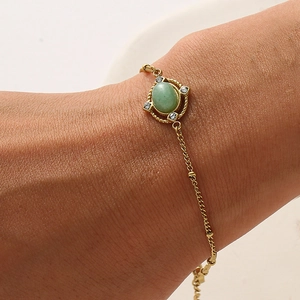 Close-up of gold chain bracelet featuring an oval green stone and zircon accents
