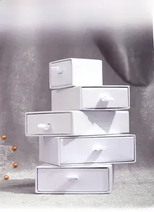 Stack of white drawer jewelry boxes with satin ribbon pulls on textured fabric