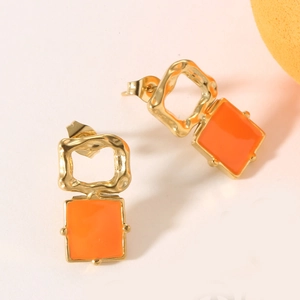 Detailed macro view of geometric earrings with hammered gold texture and orange enamel inlay