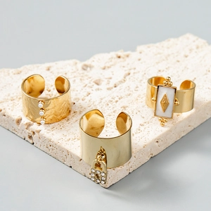 Détail de bagues dorées avec perles, breloque cadenas et insert en nacre sur pierre