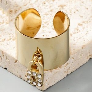 Bague large dorée avec pendentif cadenas en strass brillant sur un fond en pierre