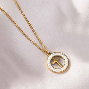 Vue macro d'un pendentif croix dorée avec cercle serti de cristaux sur de la soie