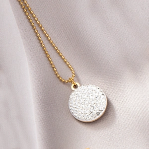 Gros plan d'un collier à perles dorées avec un pendentif rond serti de cristaux