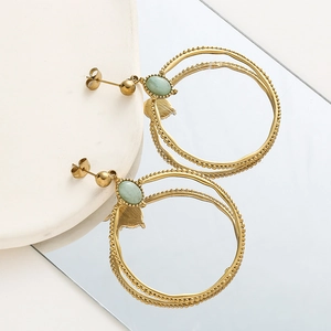 Detalle de pendientes de aro dorados con piedras verdes y textura de cuentas vintage