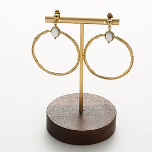 Detalle de pendientes de aro dorados con piedra blanca en soporte de joyería de madera