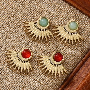 Fan-shaped gold sunburst earrings featuring natural red and green stones on linen texture