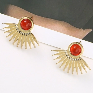 Macro view of gold fan-shaped stud earrings with red stone and sunburst pattern