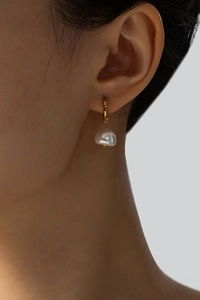 Close-up of golden hoop earrings with natural baroque pearls worn on a model ear