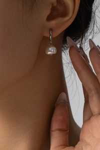 Close-up of minimalist baroque pearl earring in silver finish on model's ear