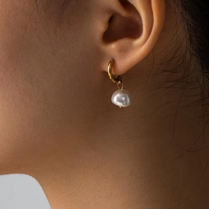 Macro shot of gold hoop earrings with natural white baroque pearl pendants worn by model