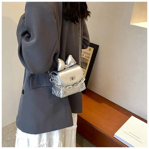 Detail of silver bow on metallic mini box bag with chain strap and glossy pleated texture
