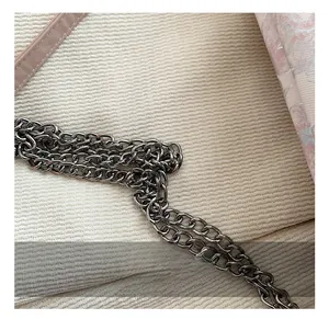 Detailed close-up of dark gunmetal chain links on a textured off-white tote bag