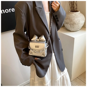 Model wearing a silver metallic mini bow bag with a sleek chain strap and fold texture