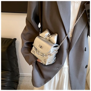 Silver metallic mini box bag featuring a large bow and chain strap on a model