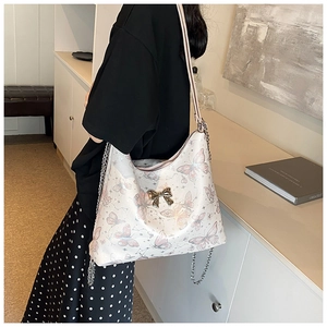 Detail of white tote bag with butterfly print and golden metal bow on shoulder strap