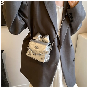 Detail shot of silver mini crossbody bag with metal chain and bow accent on model