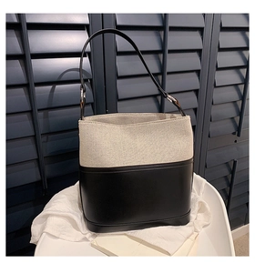 Detail of the textured beige canvas and smooth black leather bucket bag on a chair