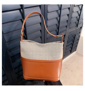 Detail of canvas bucket bag with brown leather trim against blue shutter background