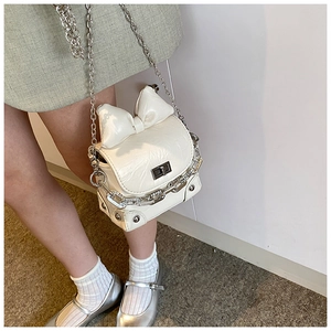 Detail of white glossy mini box bag with large bow, chunky silver chain and rivet accents